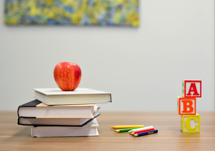 symbols of teaching, a stack of books with an apple, alphabet blocks, colored pencils, sitting on a desk